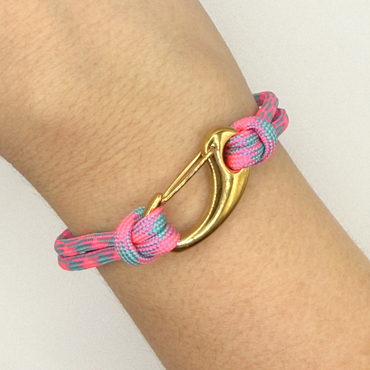 Bracelet with pink and blue cord and gold clasp on a wrist against a light background