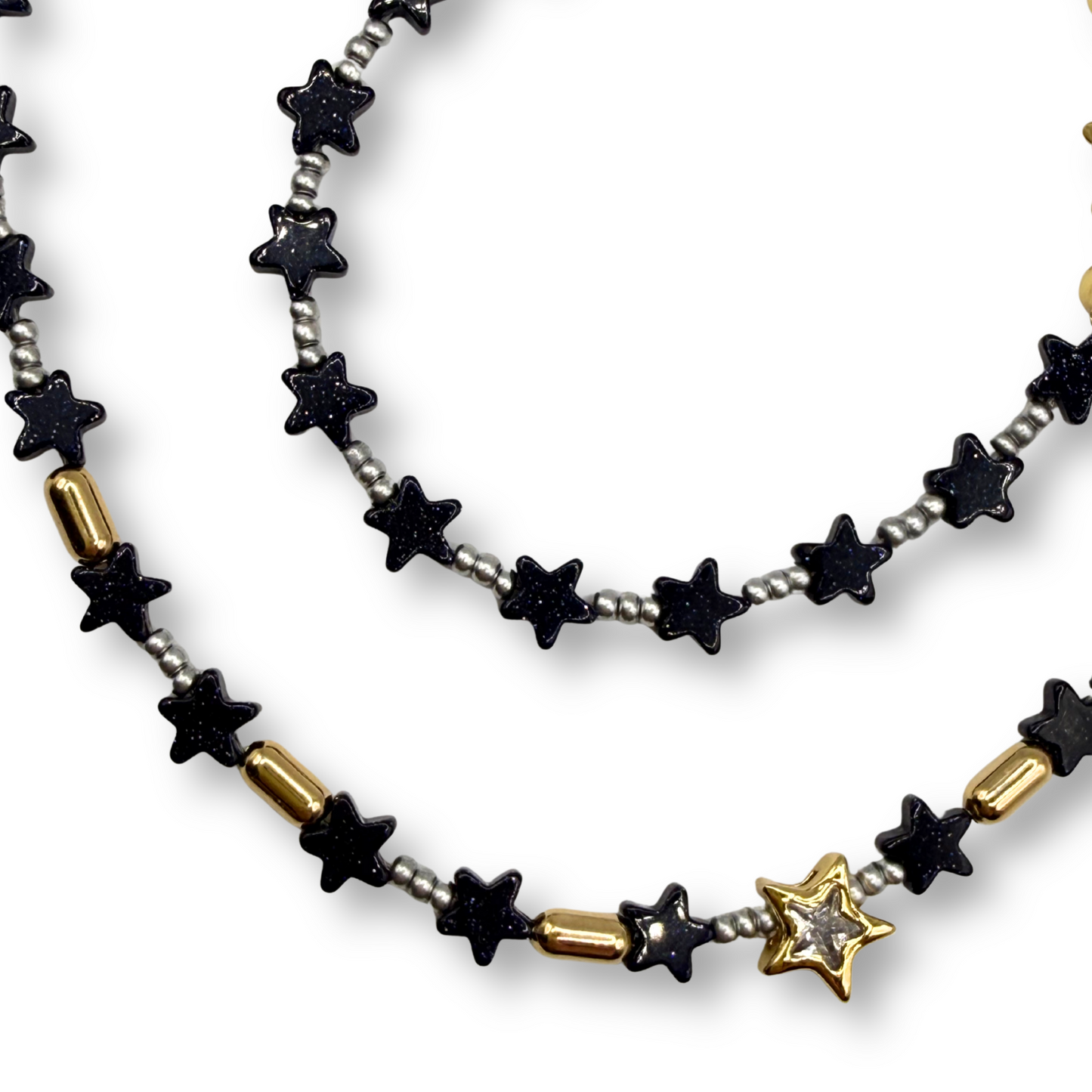 A beaded necklace featuring black star-shaped beads, small silver beads, gold cylindrical accents, and a gold star charm with a clear rhinestone, displayed on a white background.