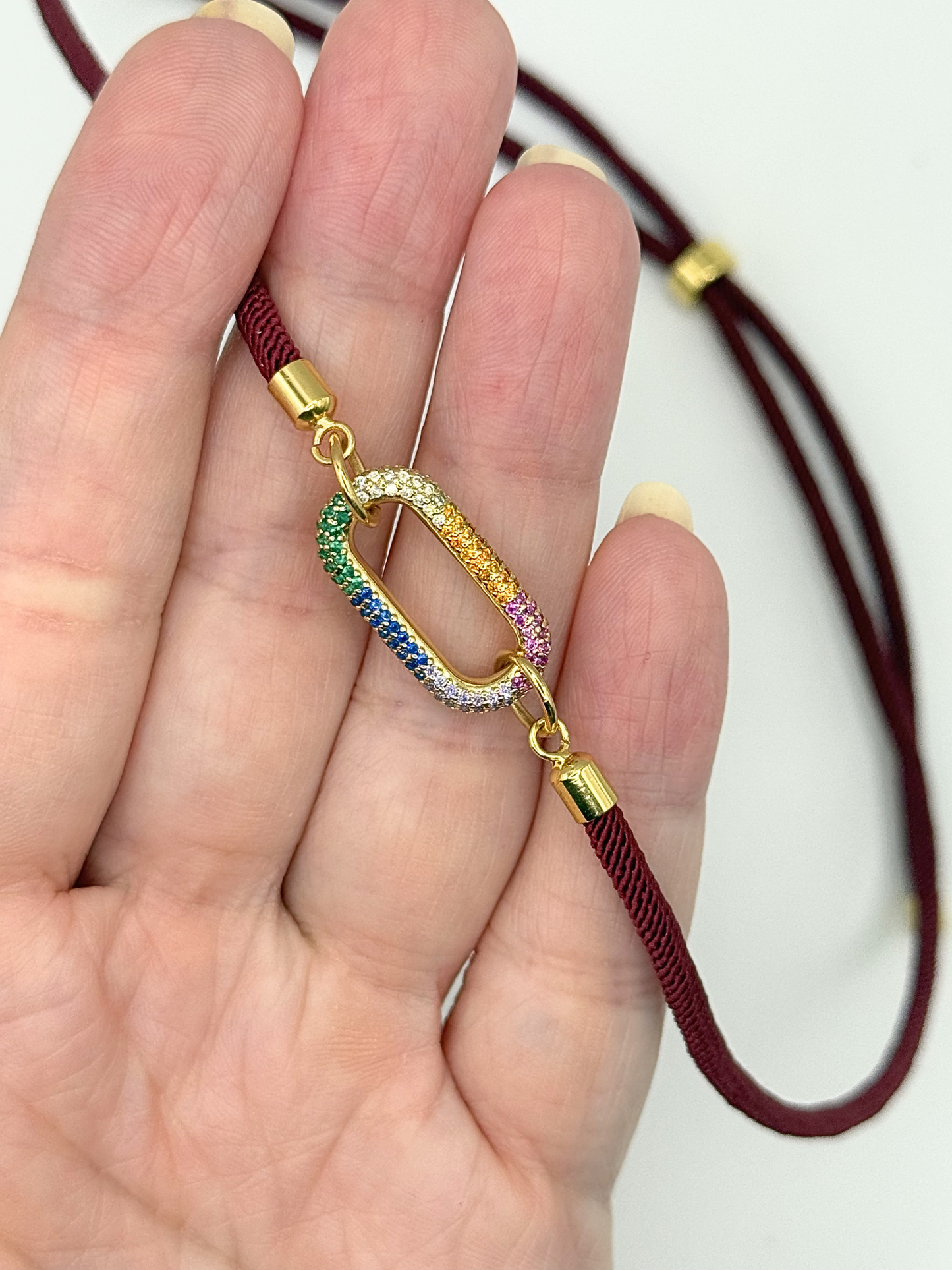 Gold bracelet with a colorful charm held in a hand against a white background