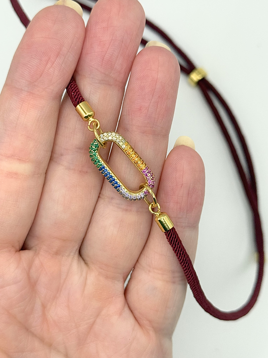 Gold bracelet with a colorful charm held in a hand against a white background
