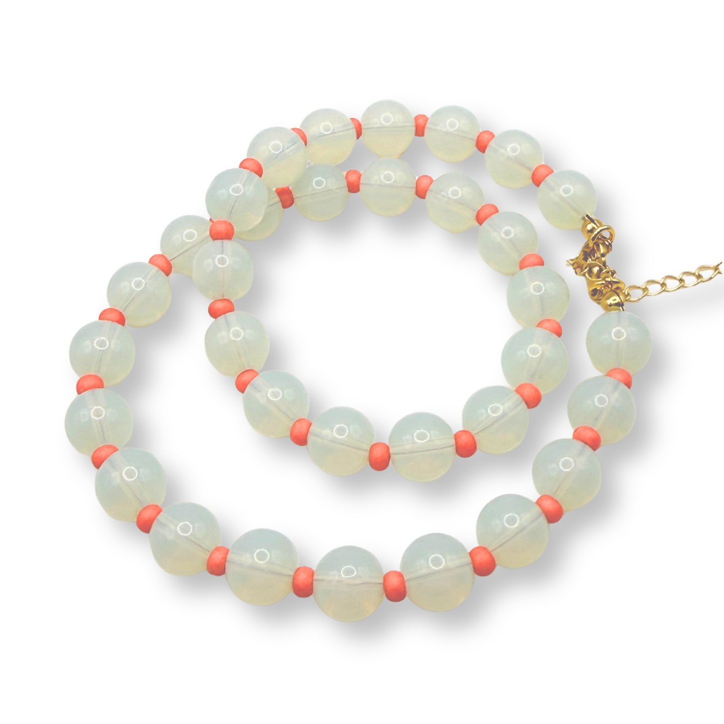 A beaded strand necklace with pale greenish-white round beads separated by small coral-pink beads, finished with a gold-tone clasp and extender chain, shown on a white background.