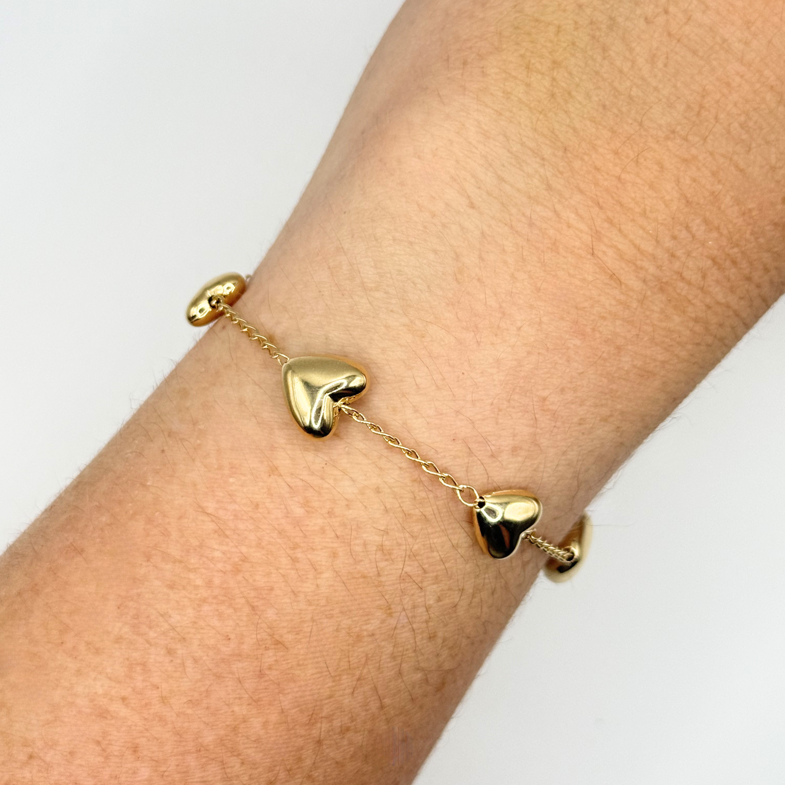 Gold heart-shaped bracelet on a wrist against a white background