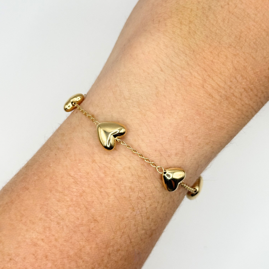Gold heart-shaped bracelet on a wrist against a white background