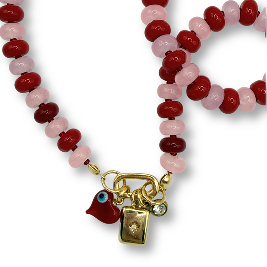 Beaded bracelet with red and pink beads and a gold charm on a white background